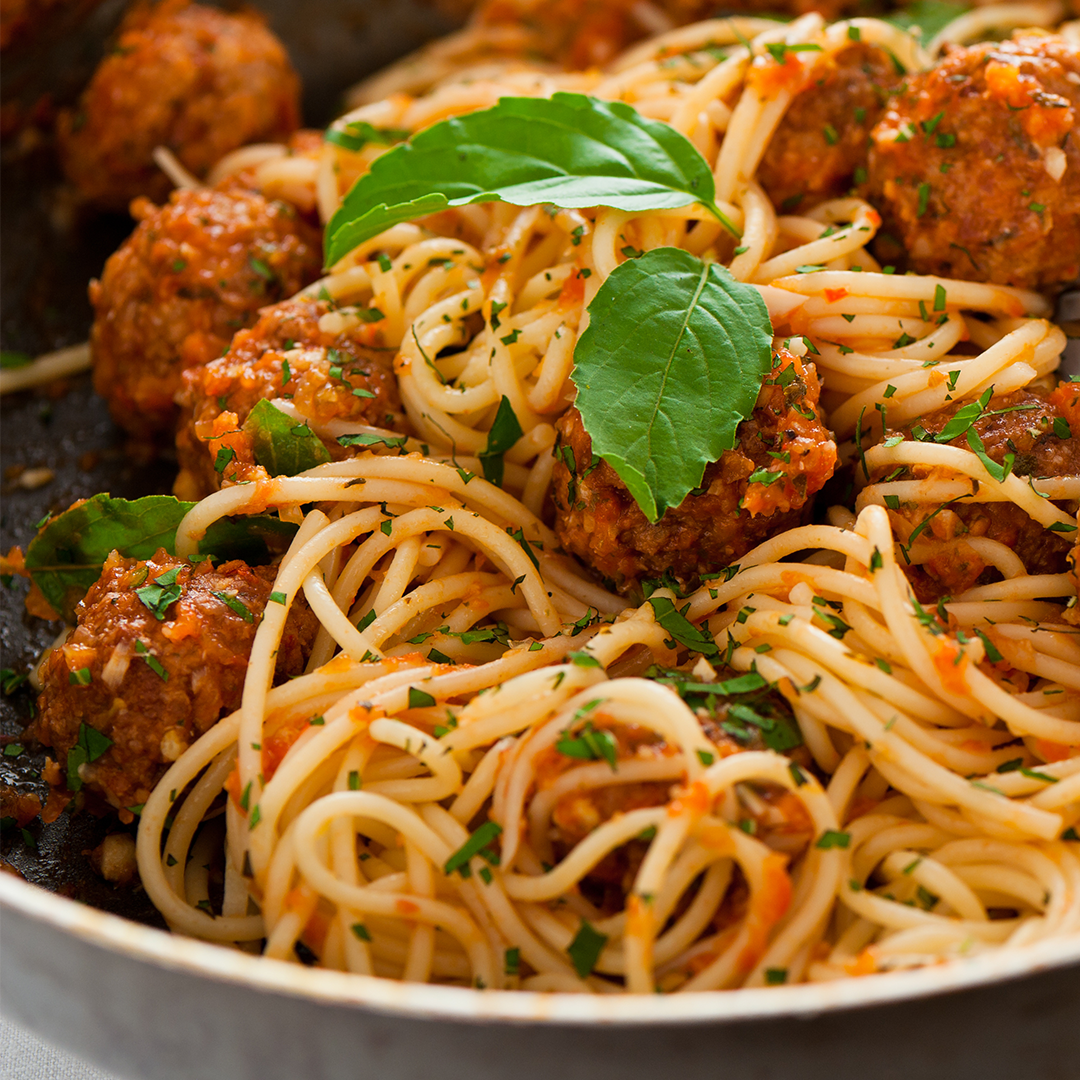 Spaghetti with meatballs in tomato sauce and fresh herbs on top