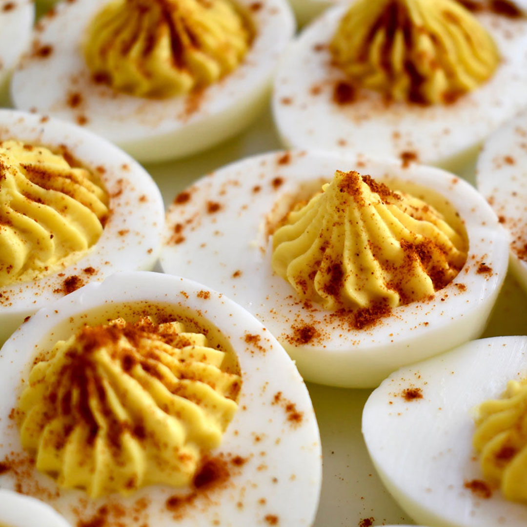 Deviled eggs with yellow piped yolk filling and paprika specks on white halves