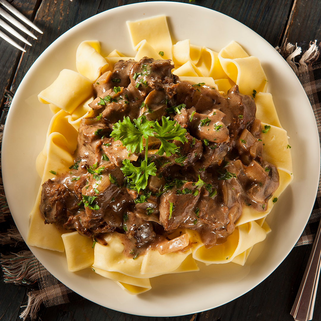 Beef stroganoff with mushrooms in a rich sauce over wide egg noodles and parsley garnish