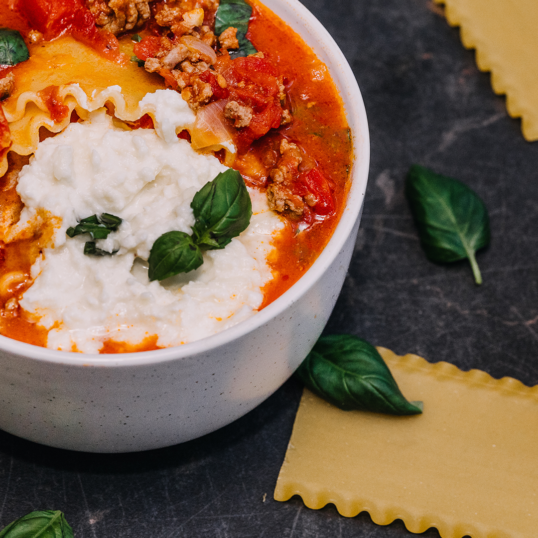 One pot lasagna pasta soup topped with ricotta and fresh basil in a white bowl