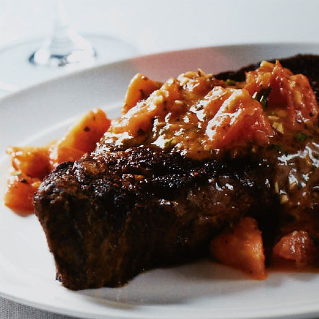 Seared New York strip topped with tomato pizzaiola sauce on a white plate