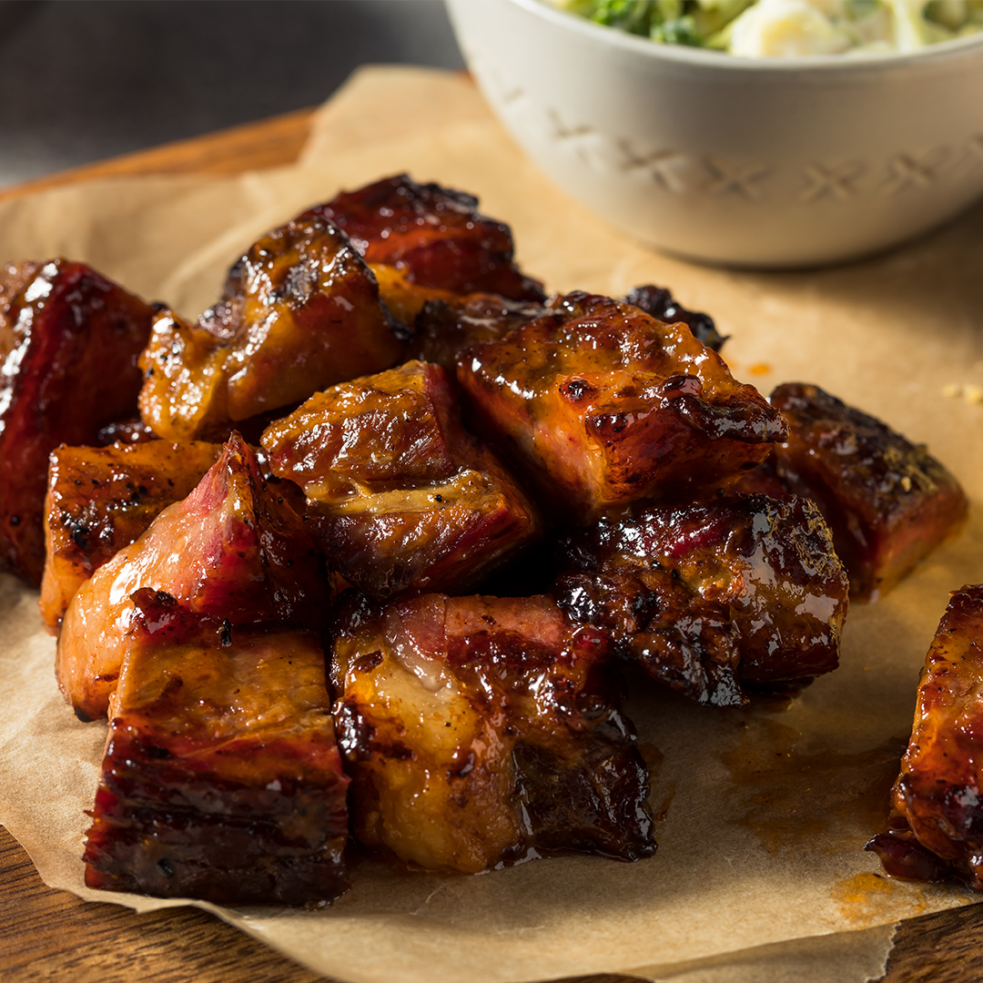 Glazed ribeye burnt ends piled on parchment with a wooden board background