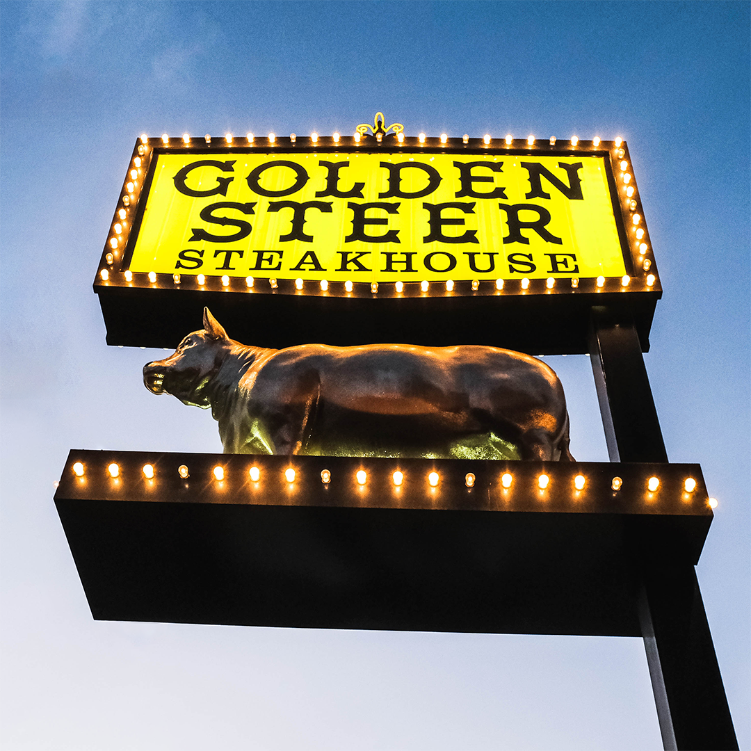 Illuminated Golden Steer Steakhouse sign with a bronze bull sculpture