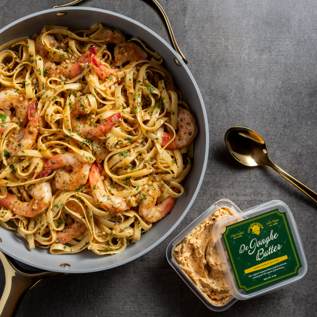Shrimp and pasta in a creamy herb sauce in a skillet with a De Jonghe Butter container nearby.
