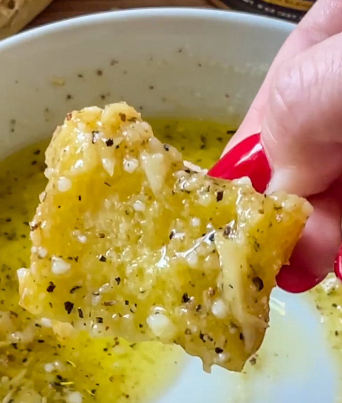 Crusty bread piece dipped into a yellow herb garlic pepper oil
