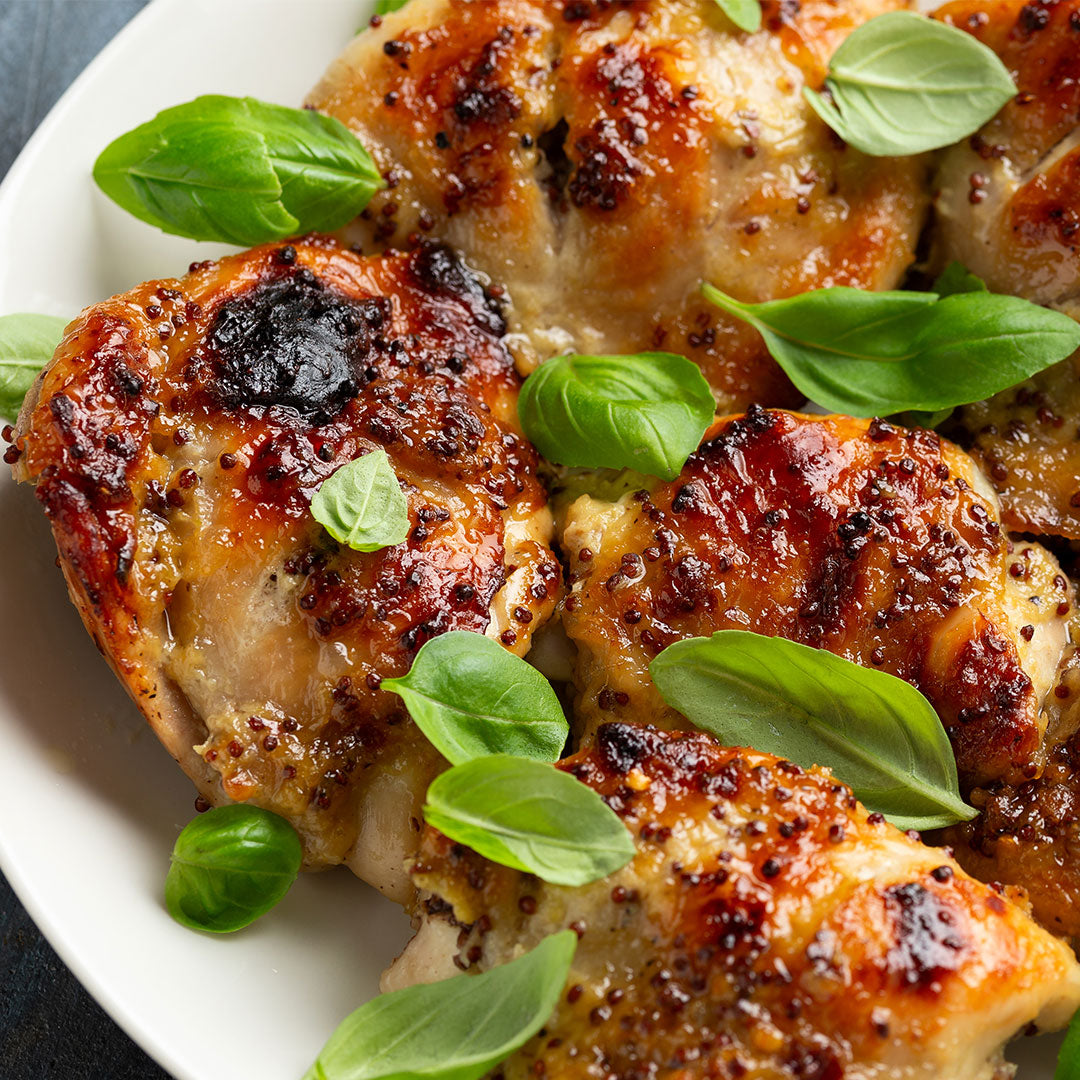 Flame grilled chicken thighs with crispy skin and fresh basil garnish