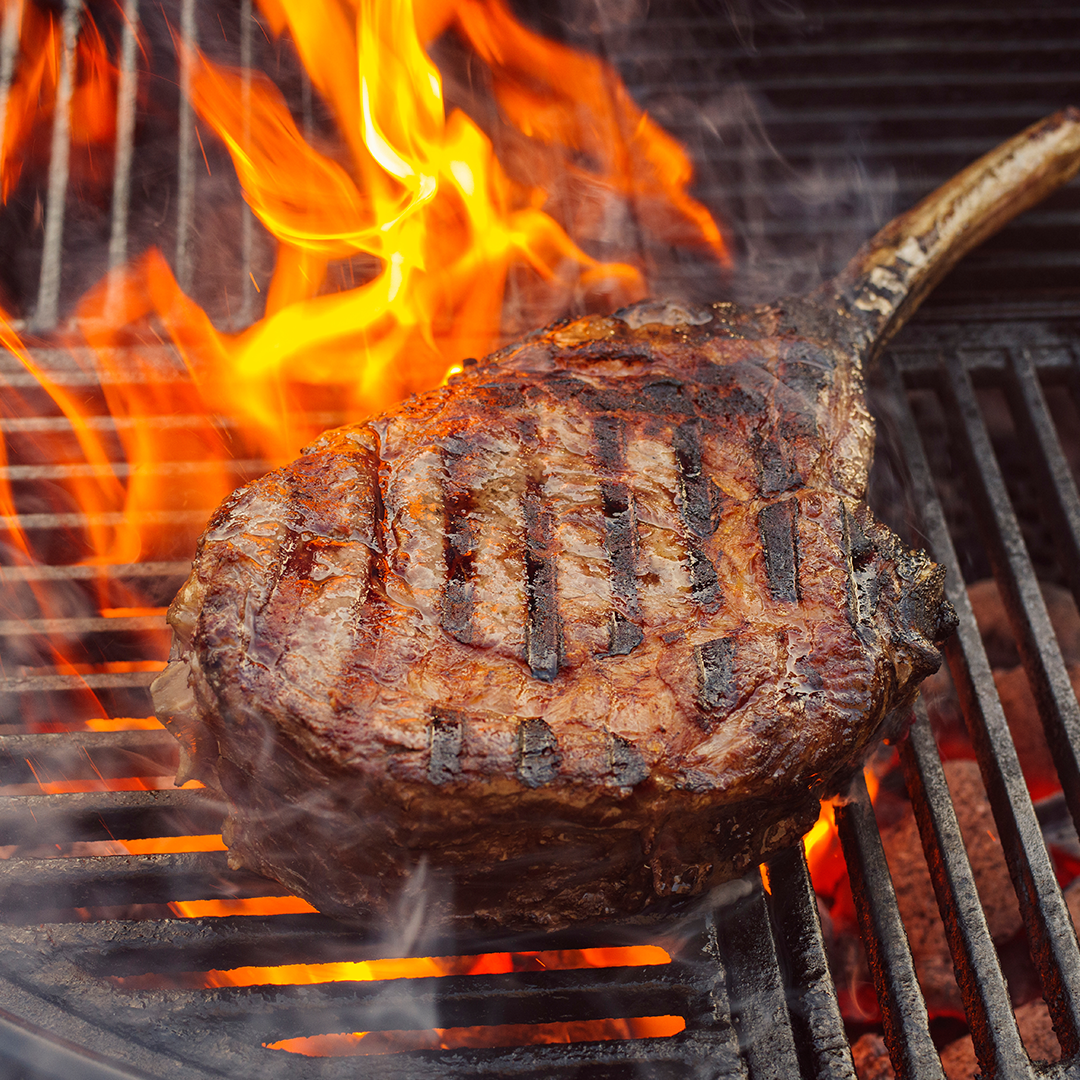 Reverse seared tomahawk steak on a hot grill with bright flames and grill marks