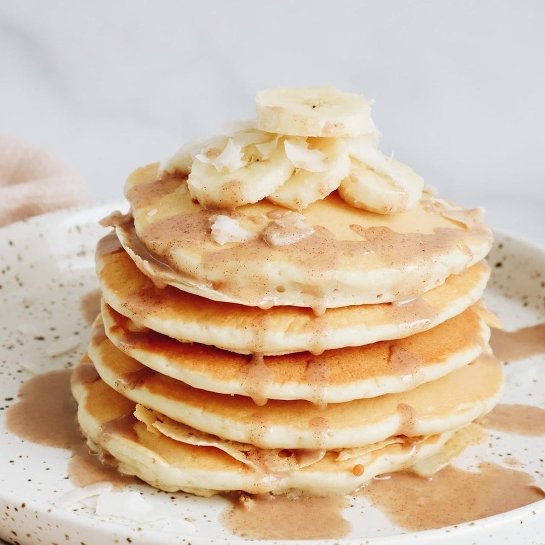 Stack of banana foster pancakes topped with banana slices and a warm sauce.