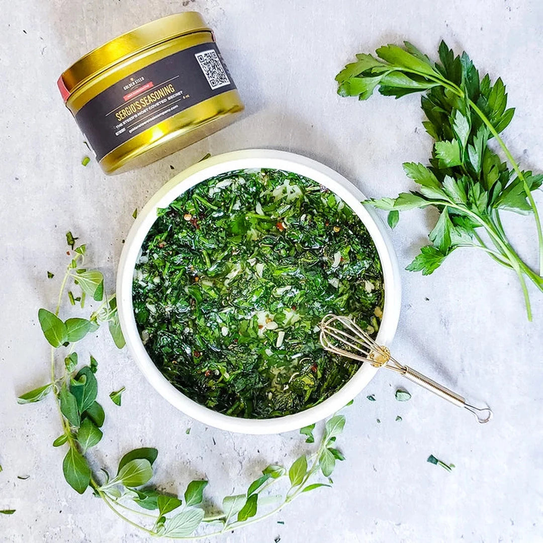 Chopped herb chimichurri in a white bowl with a Serious Seasoning tin and fresh parsley around it