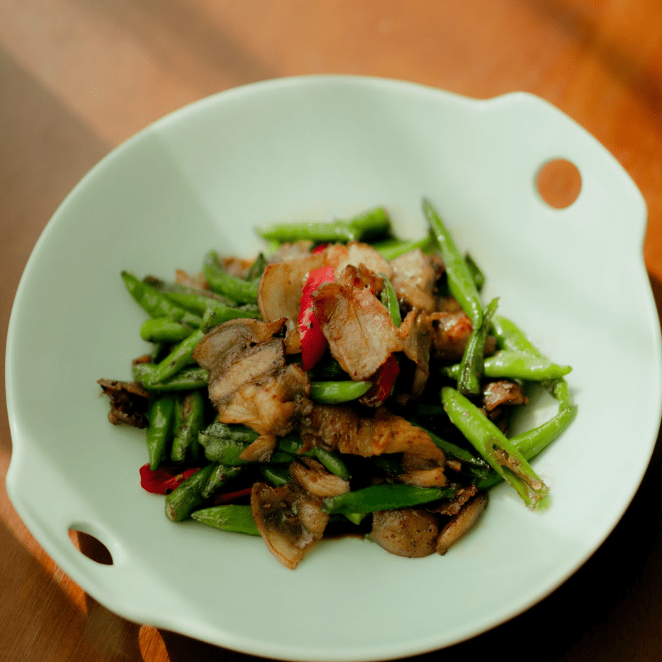 Green beans with crispy bacon and red peppers in a pale green serving bowl.