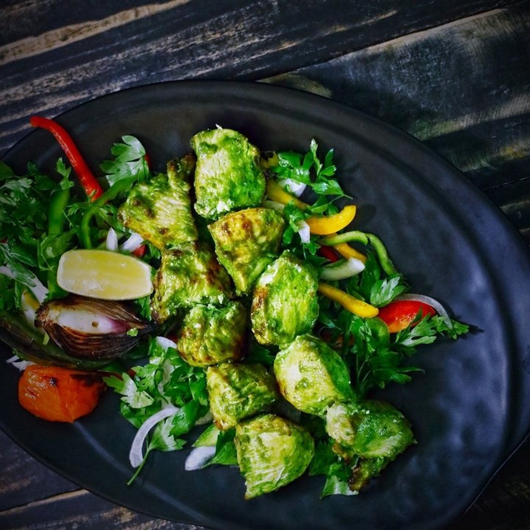 Garlic Brussels sprouts with Sergio's seasoning on a black plate with parsley and lemon wedges