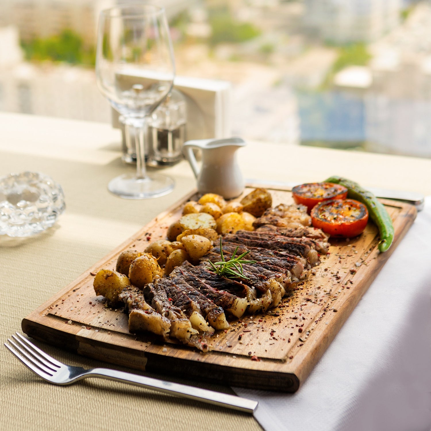 Sliced grilled ribeye steak with roasted potatoes and charred tomatoes on a wooden board.