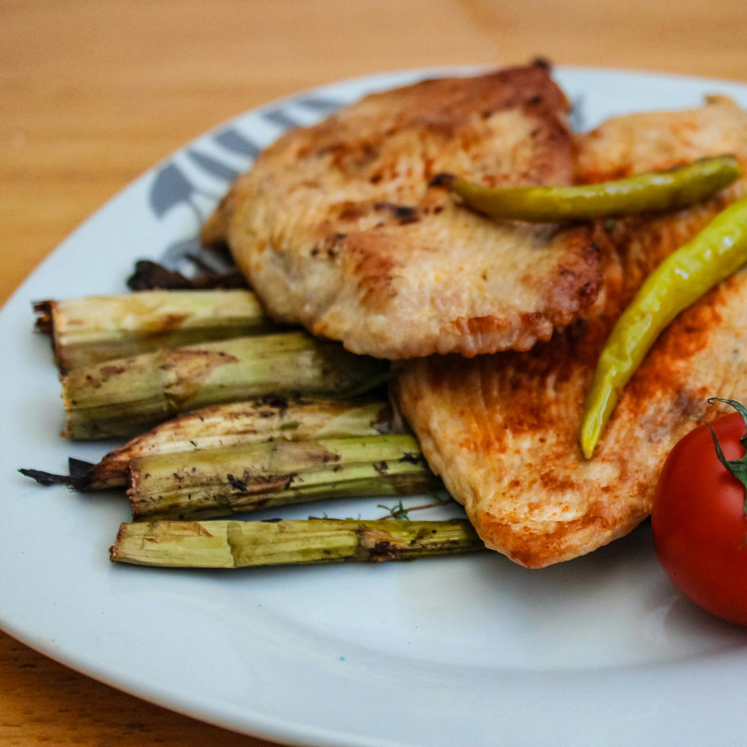 Lemon pepper seasoned chicken breasts with grilled asparagus and a tomato on a white plate