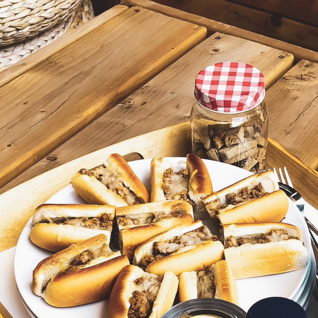 Steak and cheese subs cut into bite-sized portions arranged on a plate with a jar of seasoning in the background.