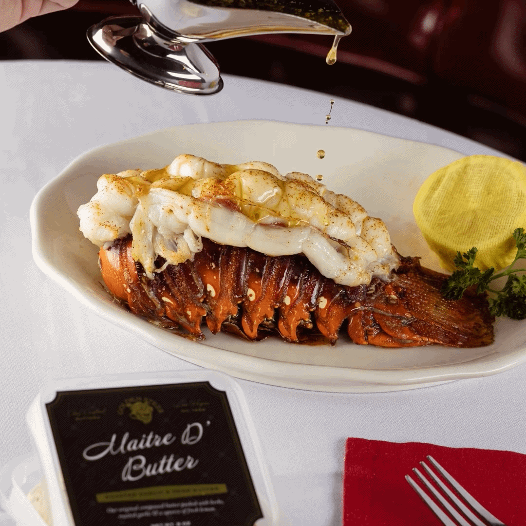 Lobster tail with white meat and butter being poured, lemon wedge on plate; branded card reads Maitre D'Butter.
