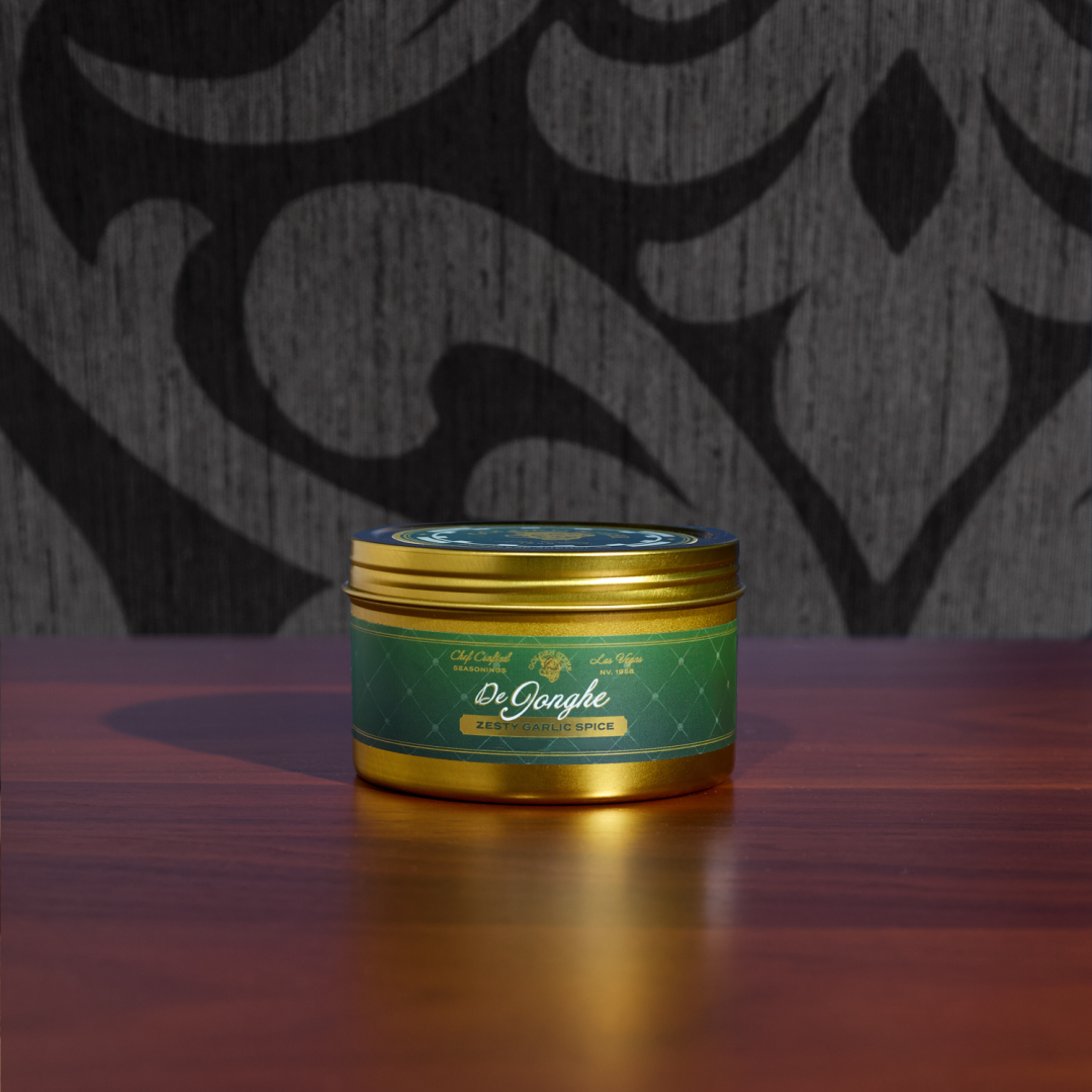 Gold seasoning tin labeled 'De Jonghe' and 'ZESTY GARLIC SPICE' on a wooden table.