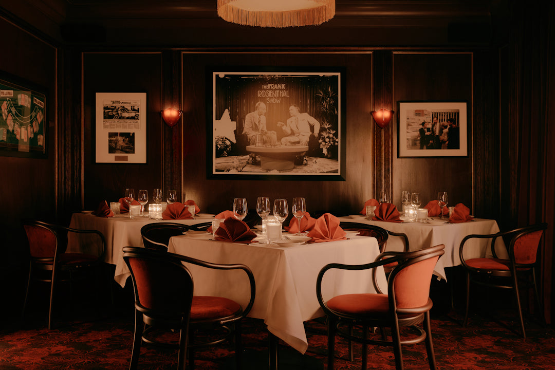 Dining room with tables set for dinner, dimly lit with framed pictures on the wall.