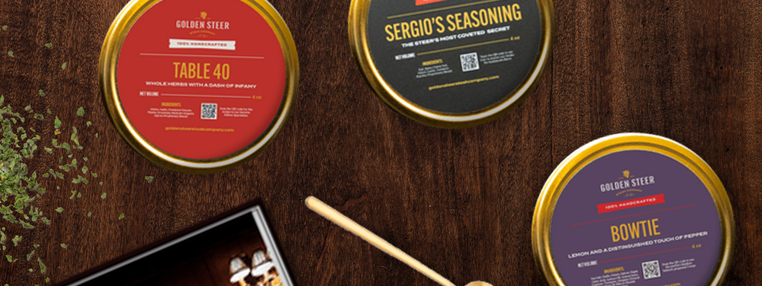 Three round Golden Steer spice tins on a wooden table labeled TABLE 40, SERGIO'S SEASONING, and BOWTIE, 100% HANDCRAFTED.