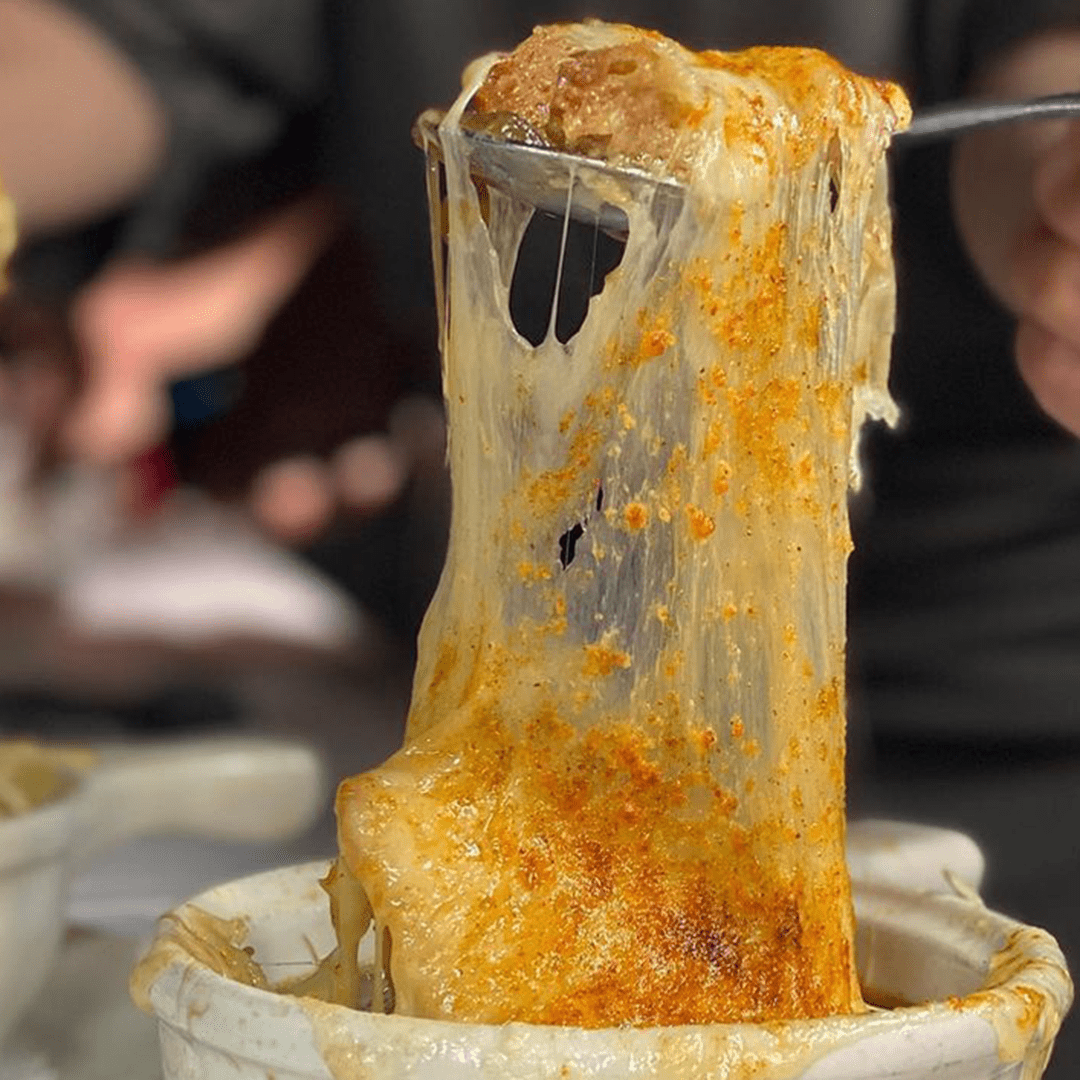 French Onion Soup with a long melted-cheese pull as a fork lifts a scoop.