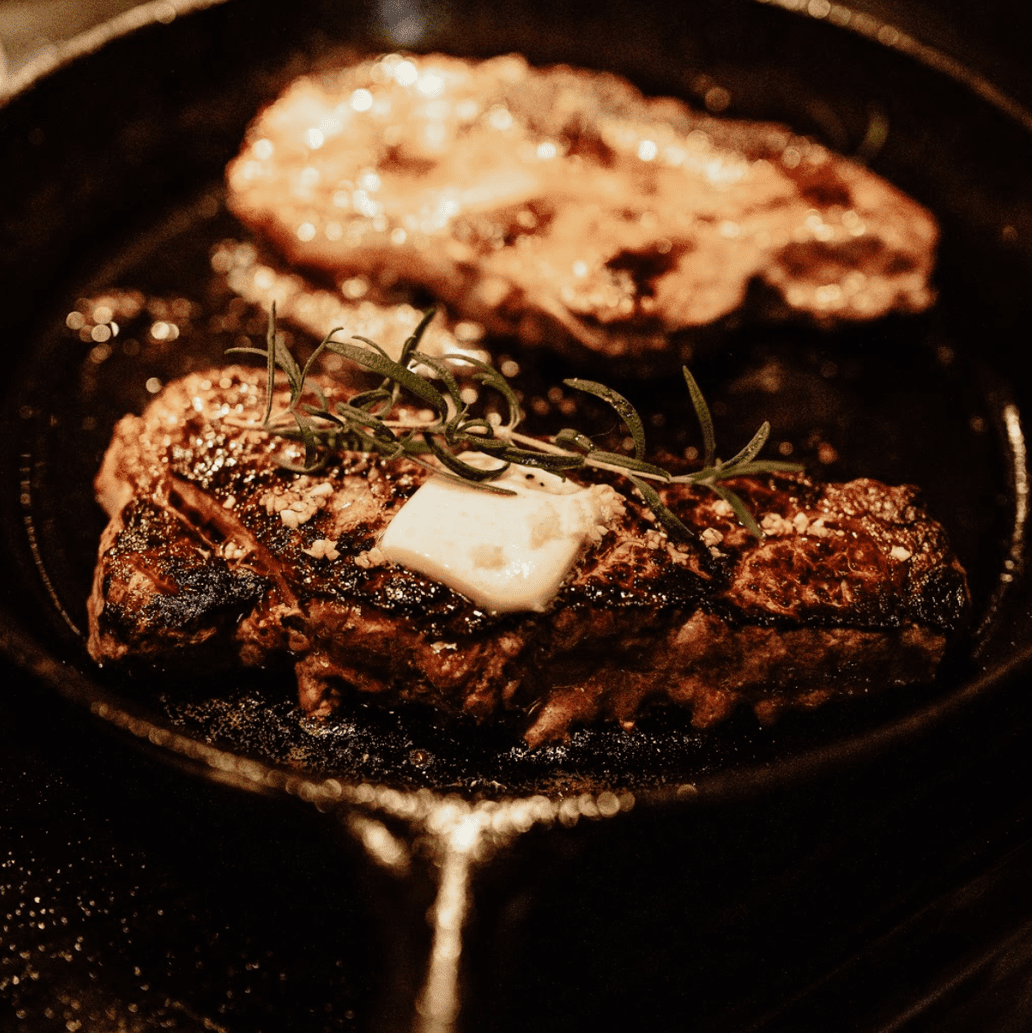 Juicy seared steak in a skillet with rosemary and a pat of butter.