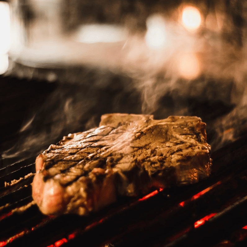 Steak searing on hot grill grates with rising smoke and glowing coals
