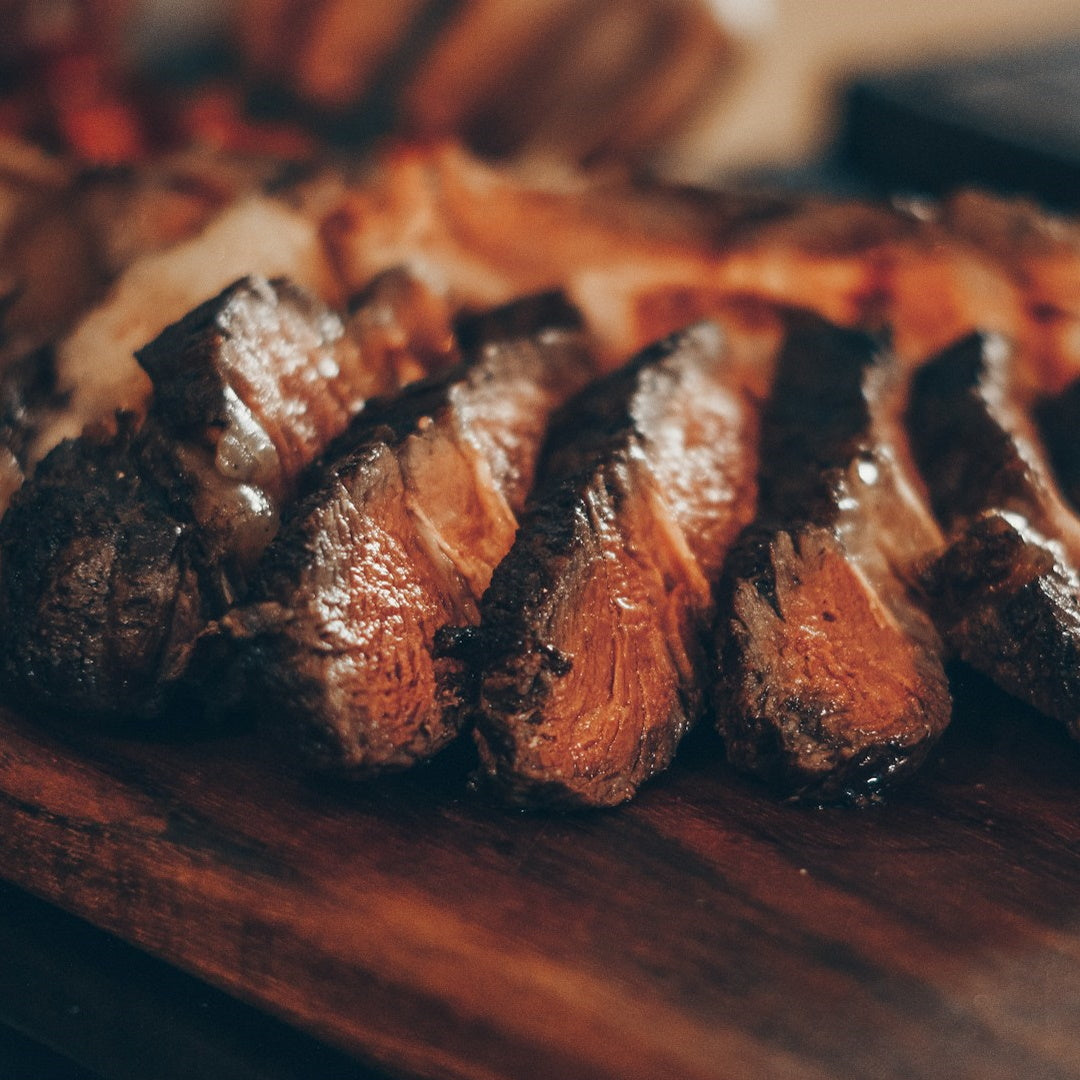 Sliced seared steak with glistening browning on a wooden cutting board