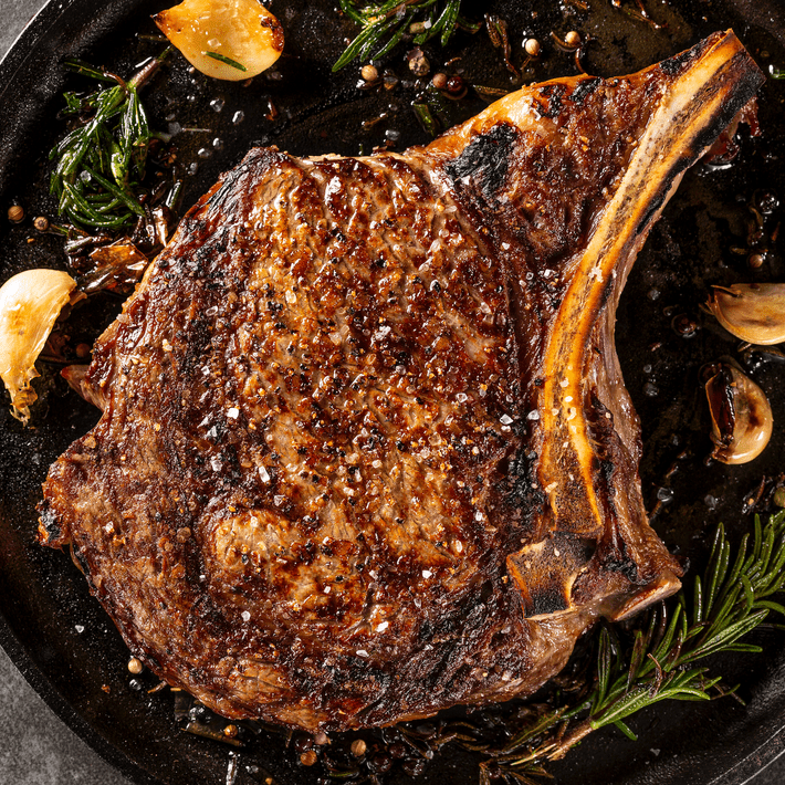 Bone-in ribeye steak seared in a cast-iron skillet with garlic cloves, rosemary sprigs, and Sergio's Seasoning