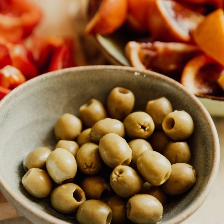 Bowl of pitted green olives with blurred appetizer bowls in the background.
