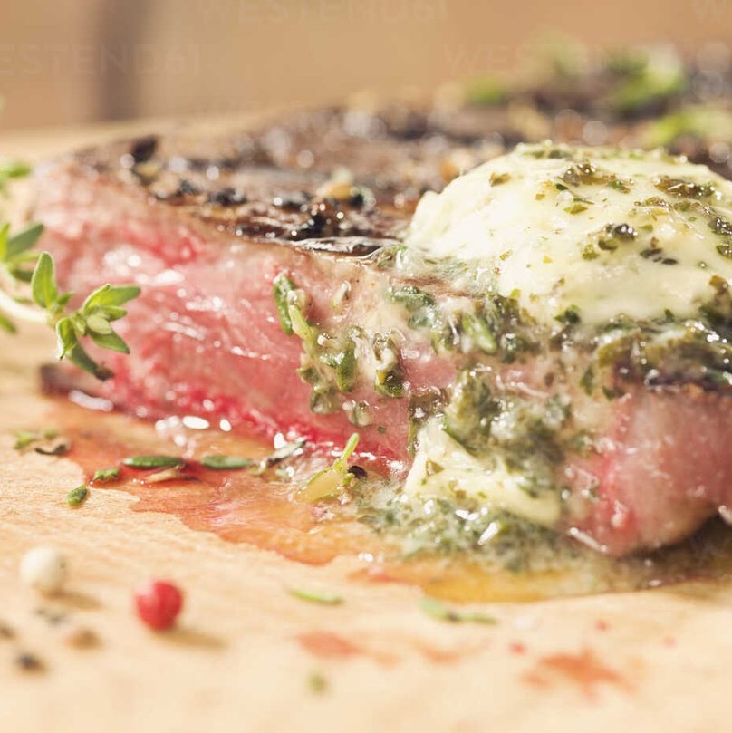 Medium-rare steak topped with melting herb butter and fresh thyme on a wooden cutting board.