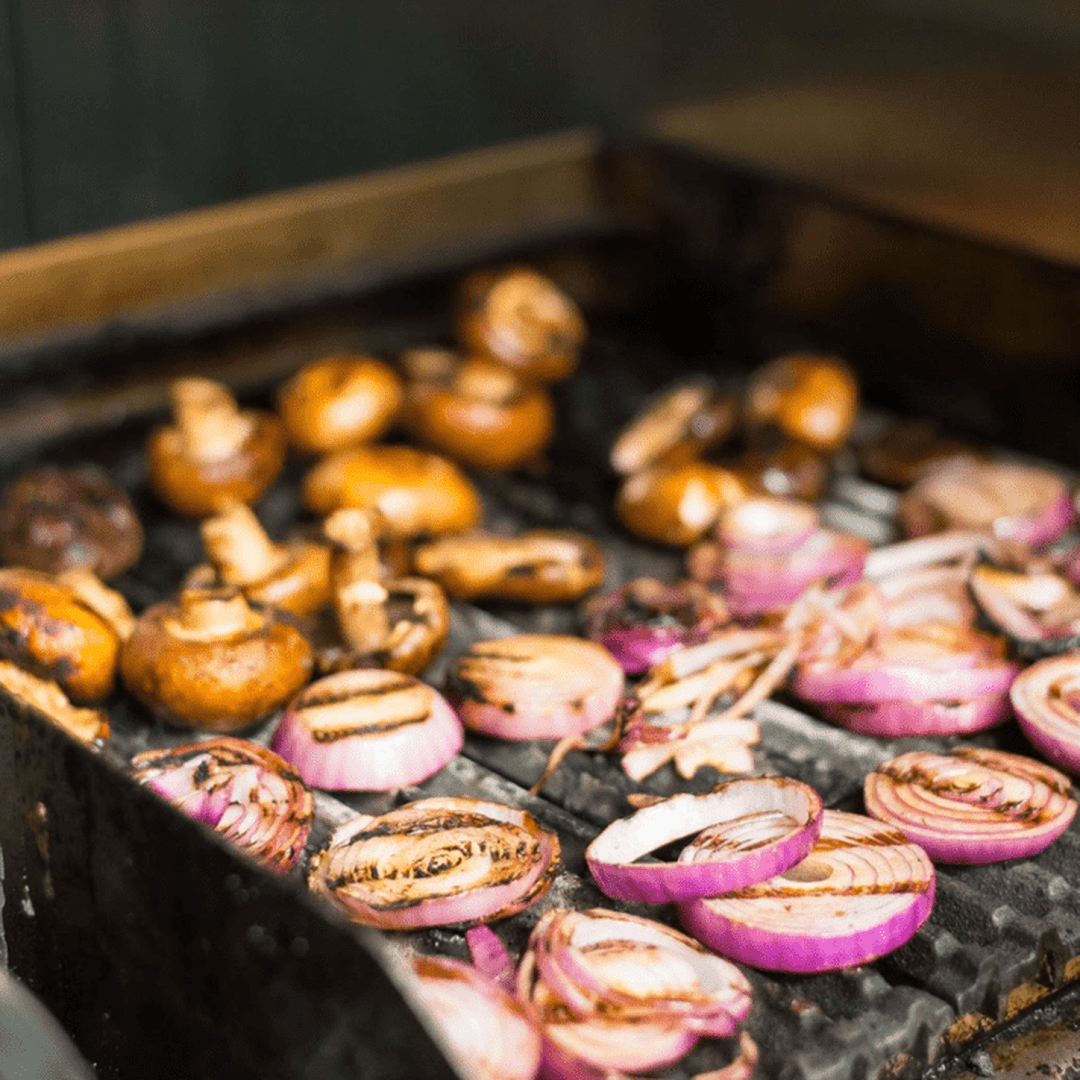 Grilled mushroom caps and charred red onion slices cooking on a hot barbecue grate