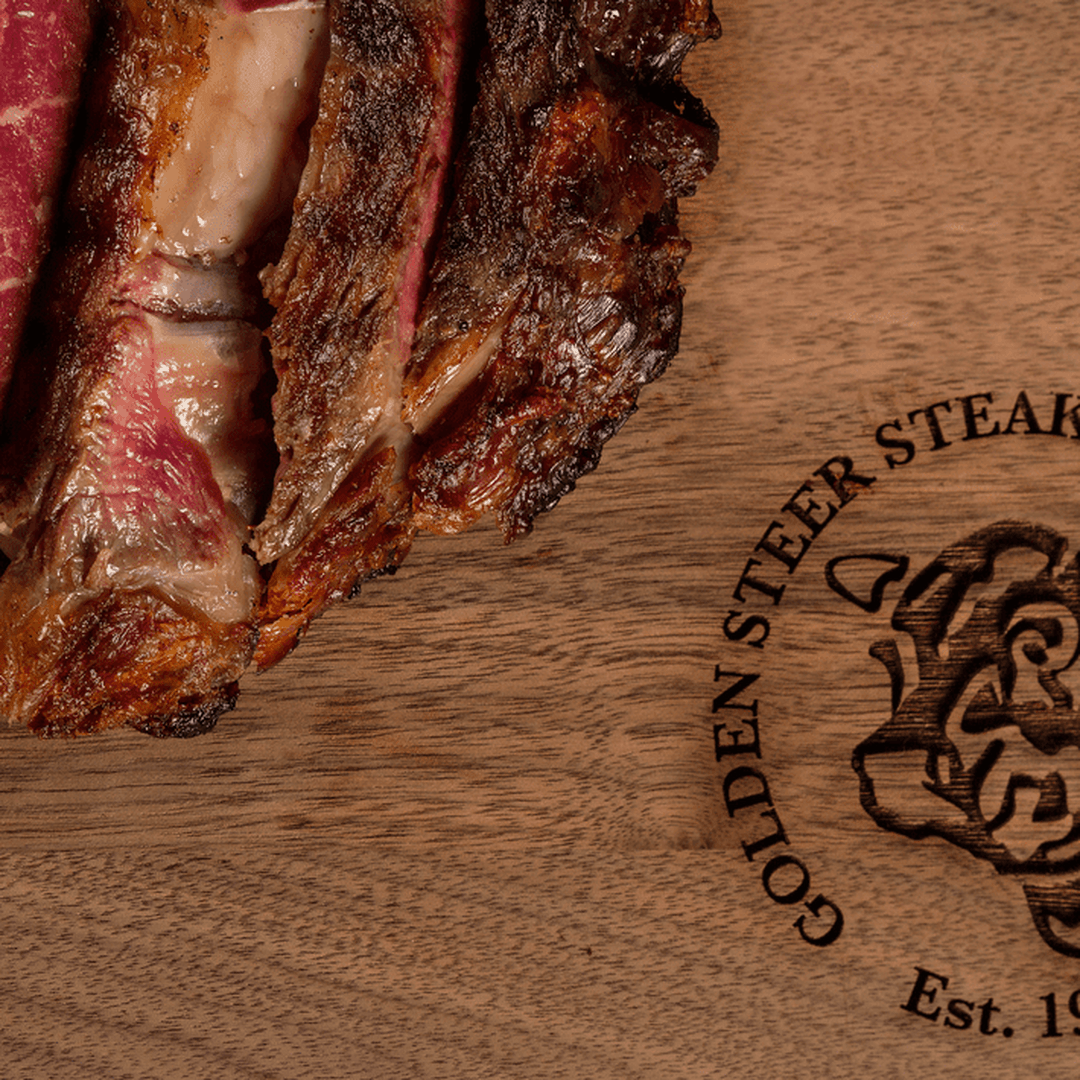 Sliced grilled tomahawk steak on a wooden cutting board stamped "GOLDEN STEER STEAK" and "Est. 19".