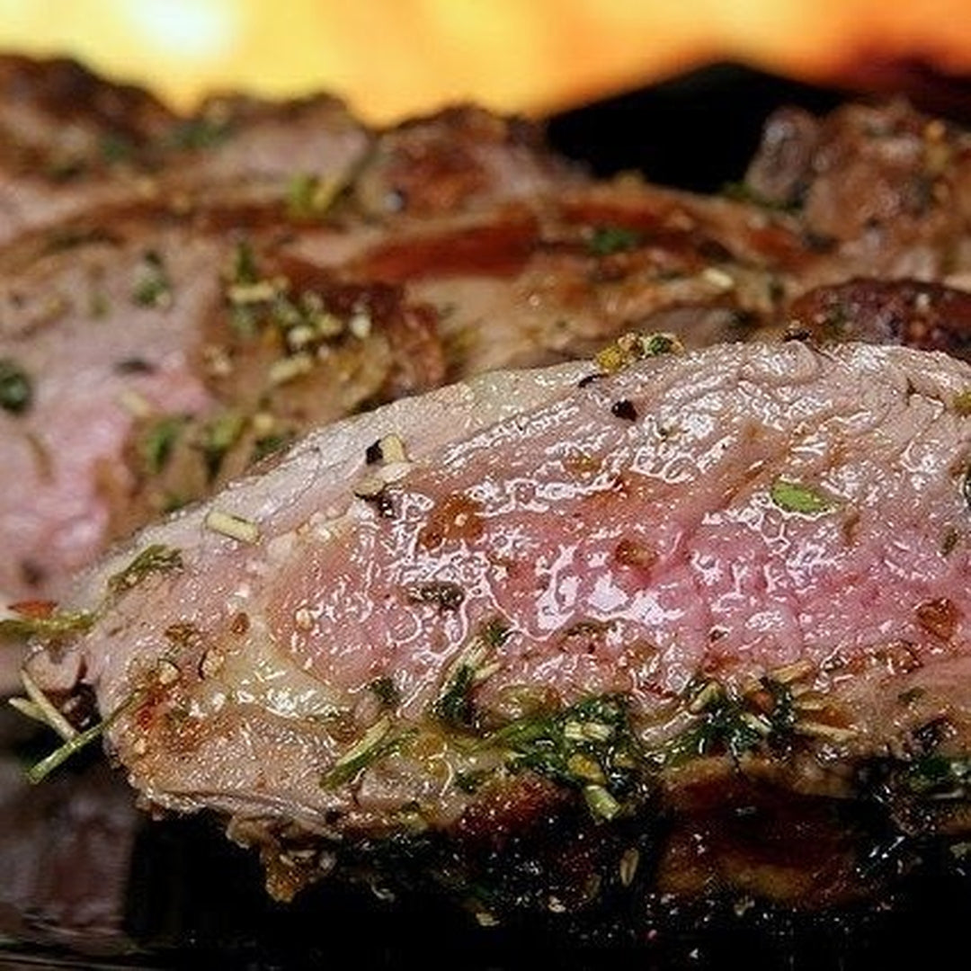Sliced medium-rare steak with herbs and juices glistening on the grill