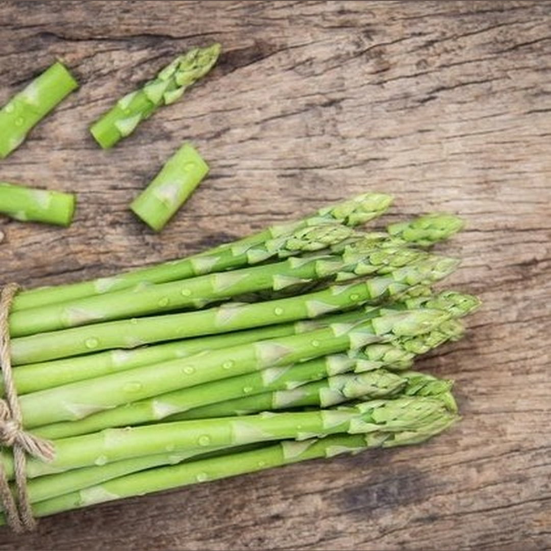 Fresh green asparagus stalks bundled with twine, water droplets on spears, laid on a rustic wooden board.