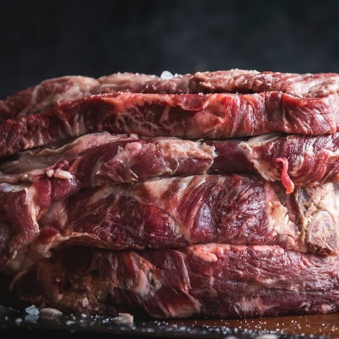 Stack of raw marbled steak cuts on dark background sprinkled with coarse salt