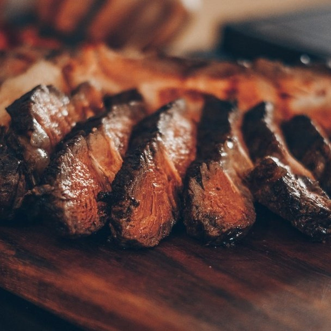 Close-up of sliced, medium-rare steak with seared crust arranged on a wooden cutting board.