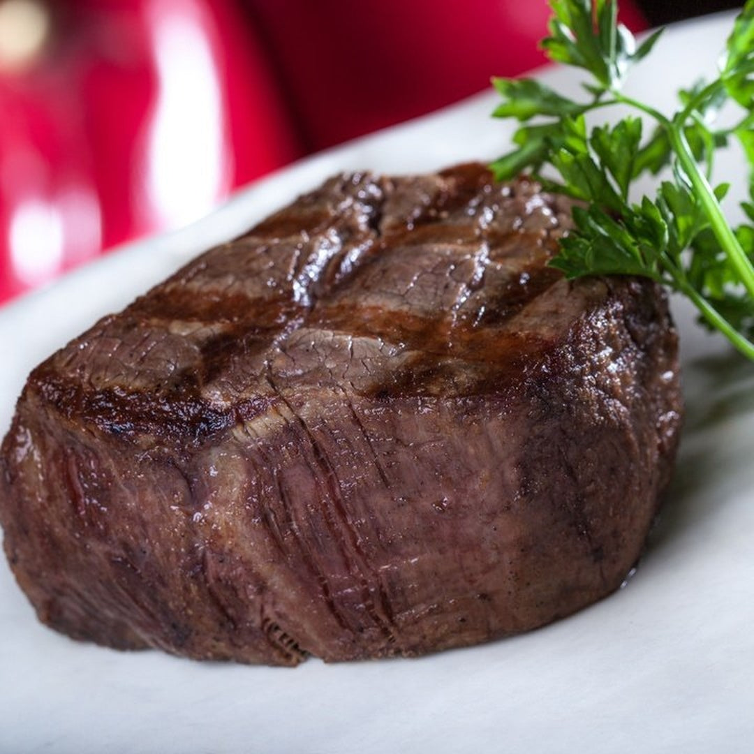 Grilled filet mignon with seared grill marks on a white plate, garnished with parsley