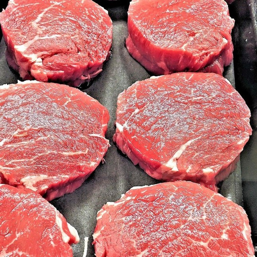Six round beef steaks with light white marbling, arranged in two columns on a black tray