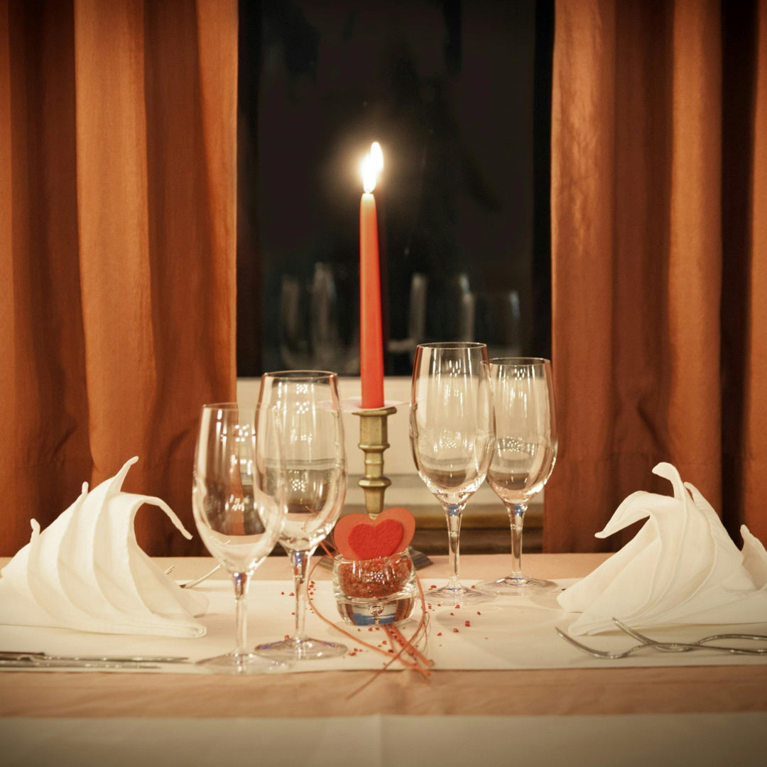 Romantic table setting with lit red taper candle, wine glasses, folded napkins and small red heart decoration