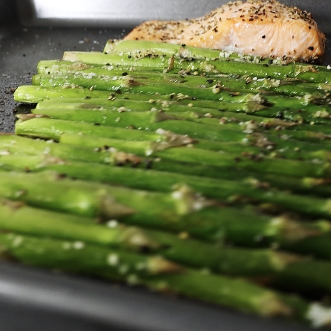Roasted asparagus spears seasoned with herbs and pepper beside a seared salmon fillet