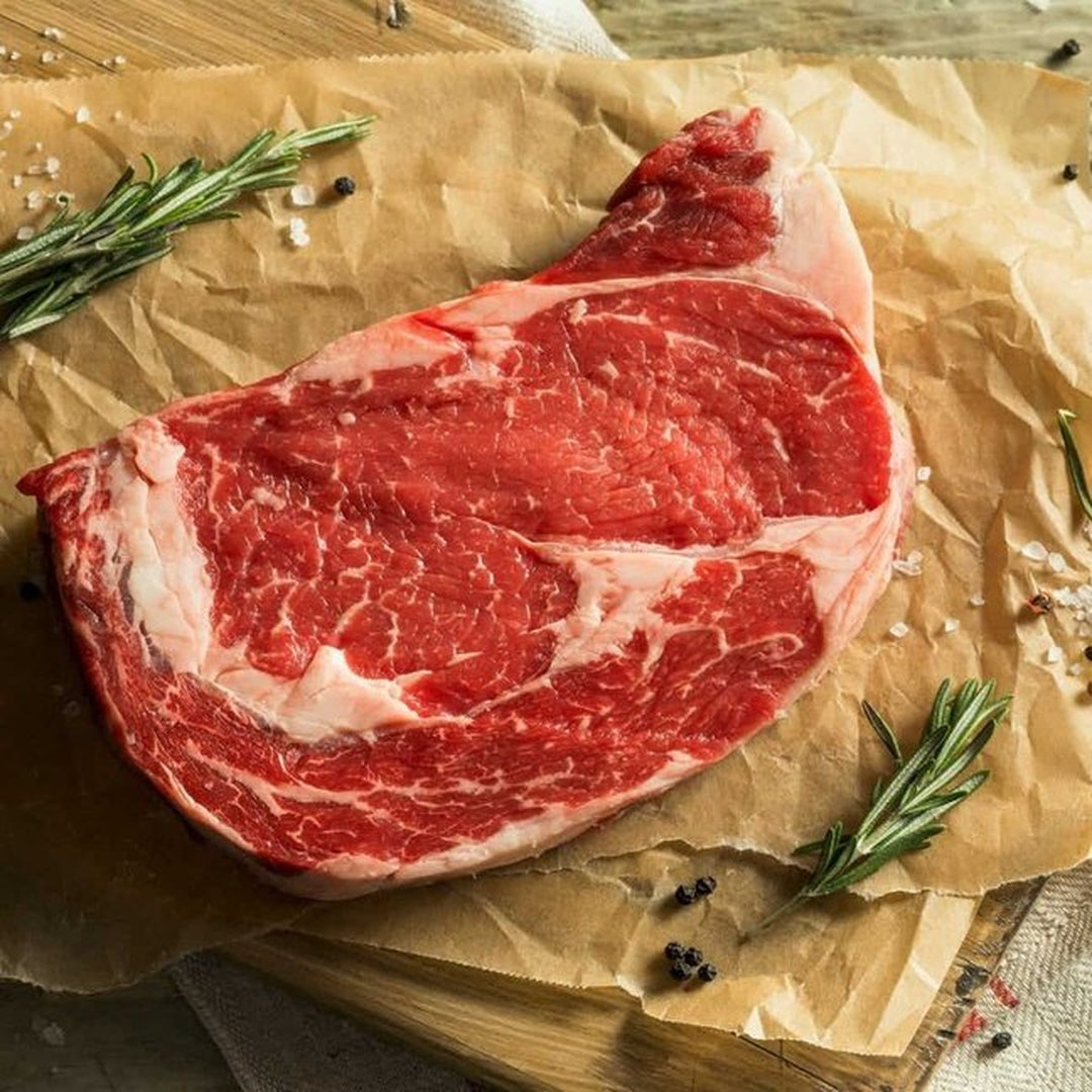 Raw ribeye steak on parchment with rosemary sprigs, coarse salt and peppercorns