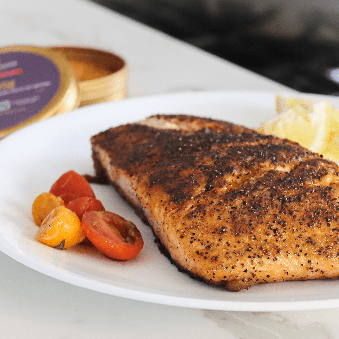 Blackened salmon fillet on a white plate with cherry tomatoes and a lemon wedge