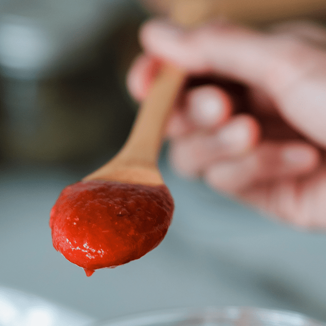 Wooden spoon holding classic marinara sauce with a drop forming at the tip