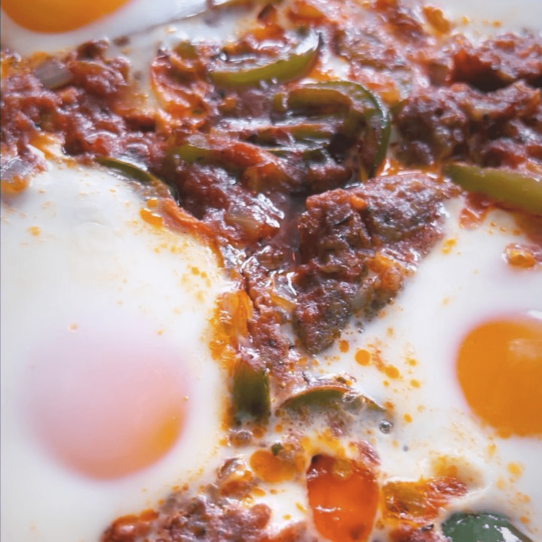 Two eggs simmering in spicy tomato-pepper sauce with sliced green peppers and bright yolks