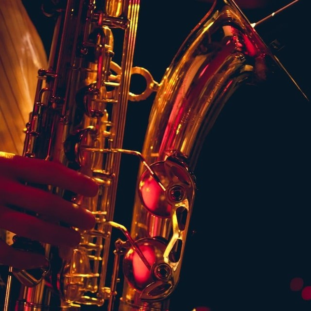 Close-up of a saxophone's curved body, keys and a player's left hand under warm red-gold stage lighting.