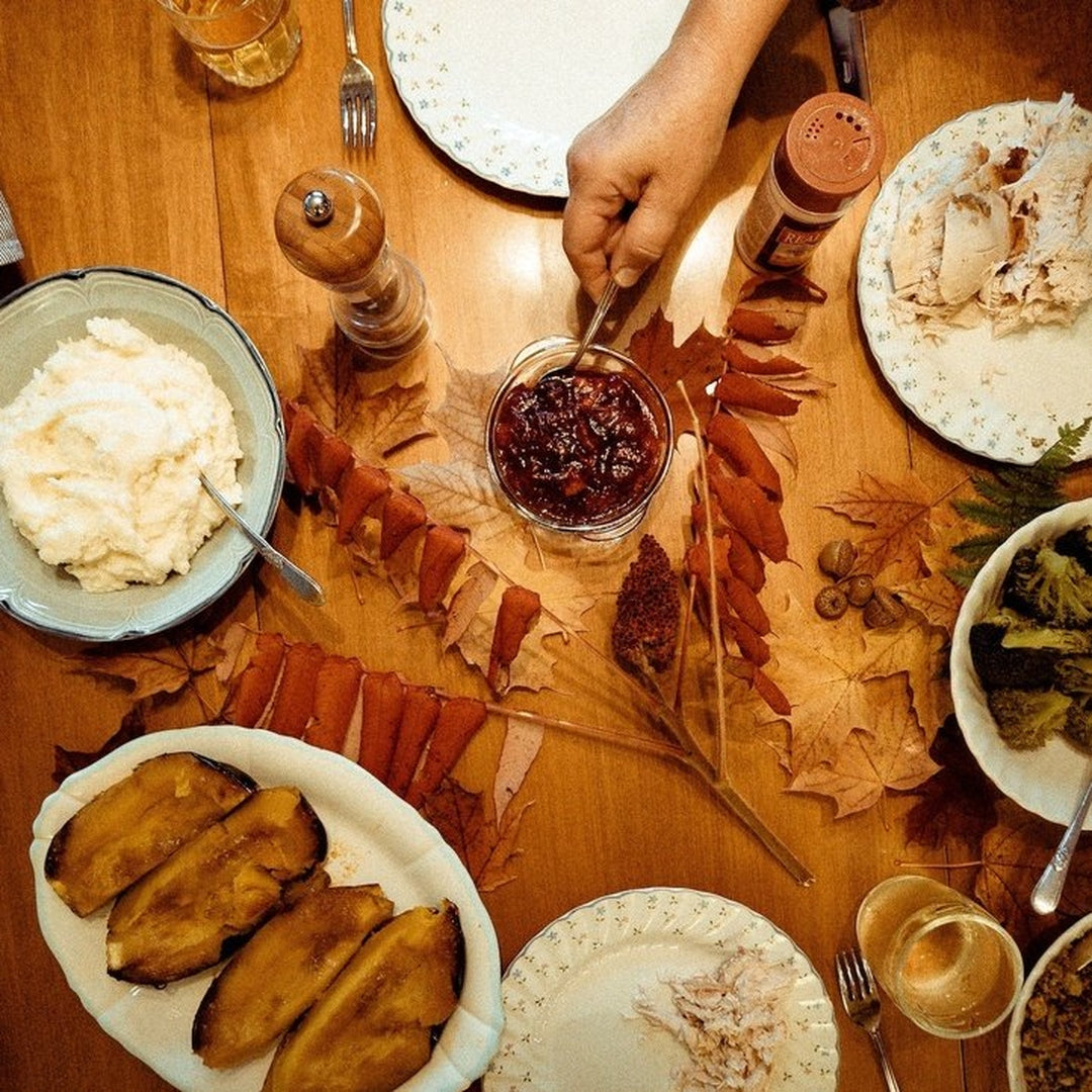 Overhead Thanksgiving table with mashed potatoes, sweet potatoes, cranberry sauce spooned, carved turkey, greens, fall leaves.