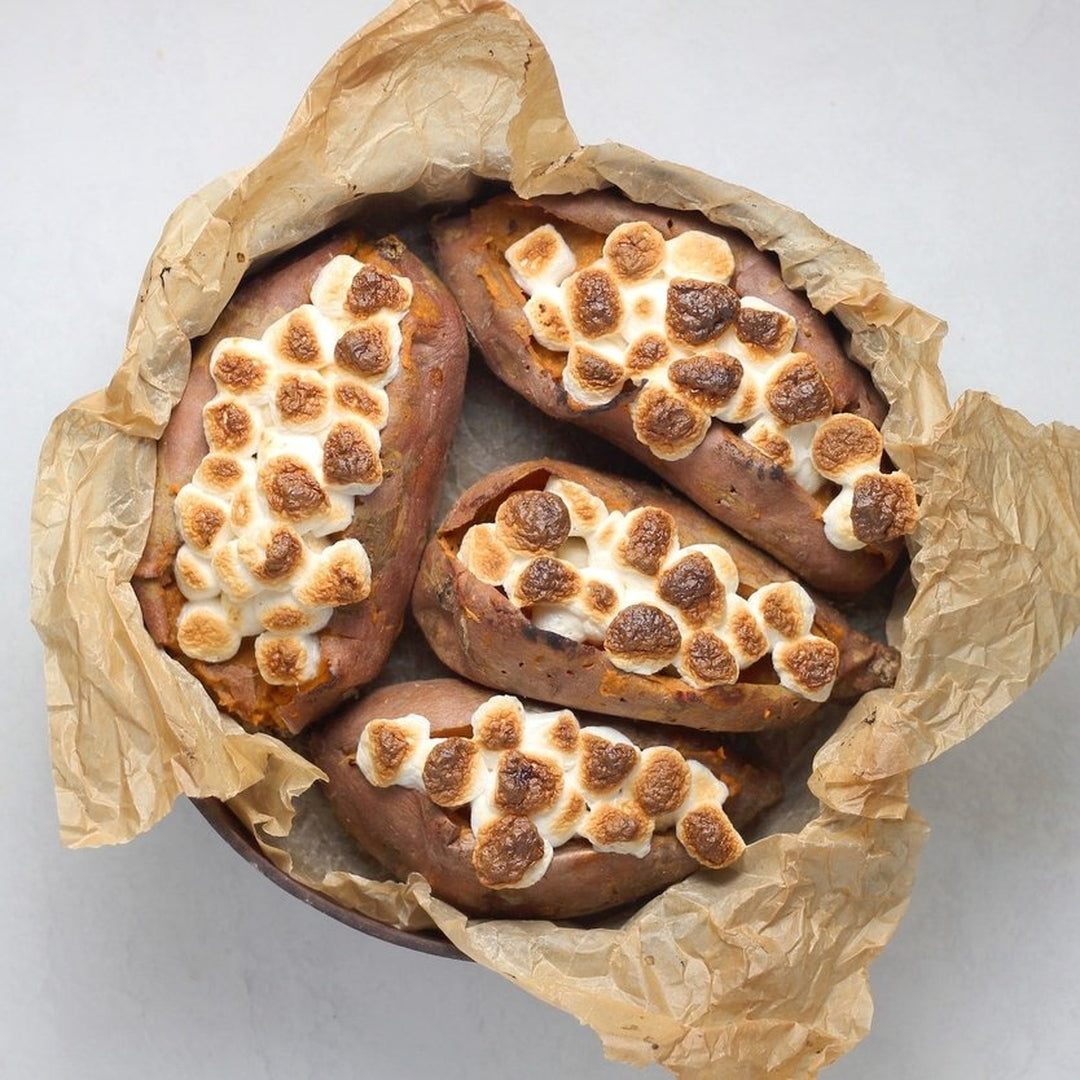 Baked sweet potatoes split and filled with toasted marshmallows, served in a parchment-lined bowl