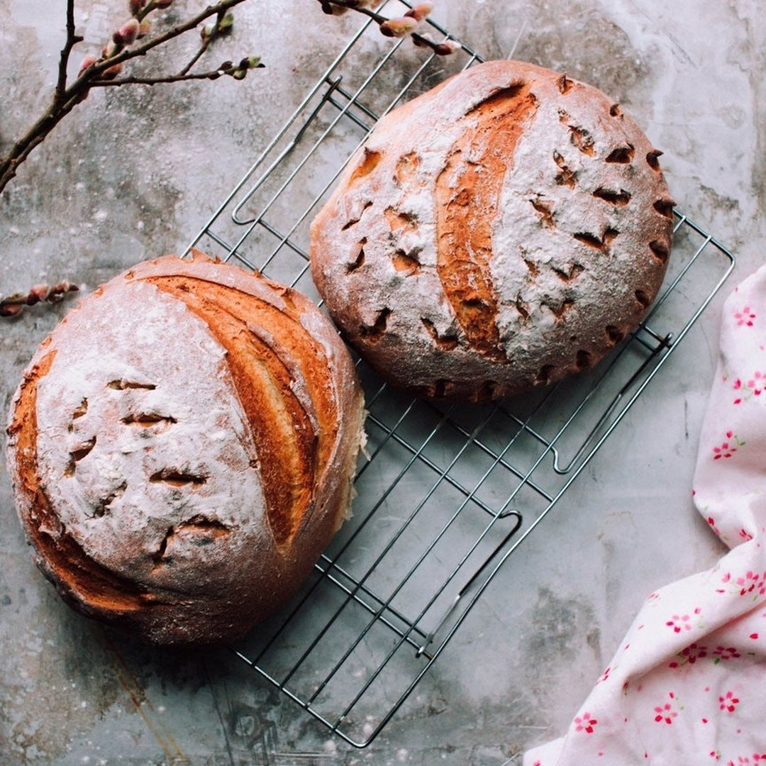 Two round crusty loaves dusted with flour on a wire cooling rack beside a floral cloth