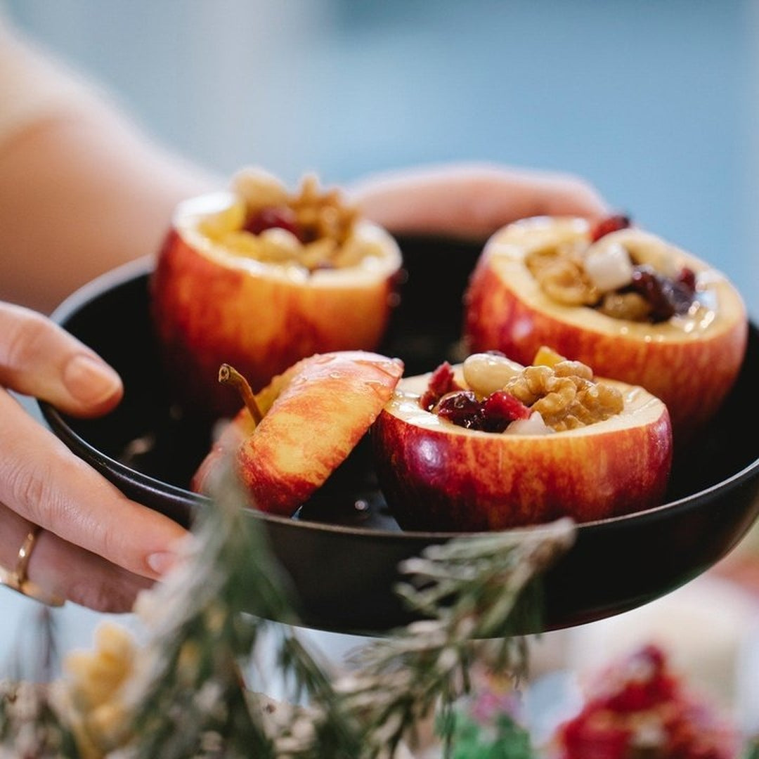 Baked apples hollowed and stuffed with walnuts and cranberries, served in a black pan held by a hand
