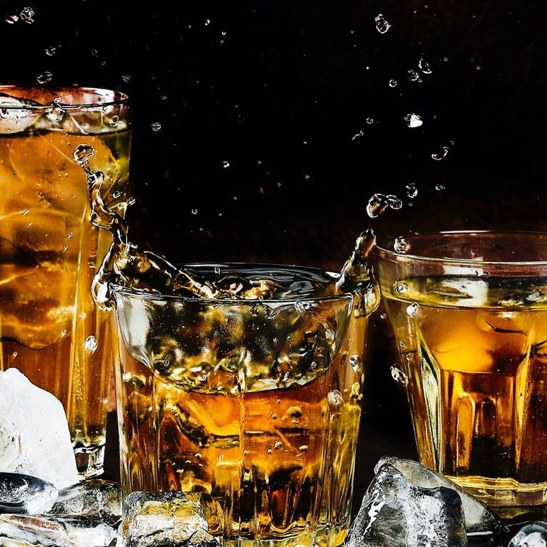 Three amber cocktails in lowball glasses splashing over ice against a dark background