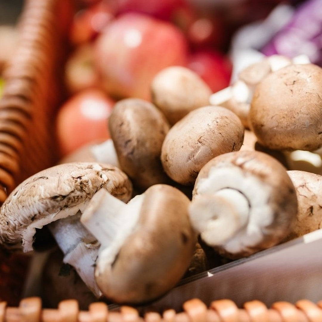 Close-up of cremini mushrooms in a woven basket with blurred apples in the background
